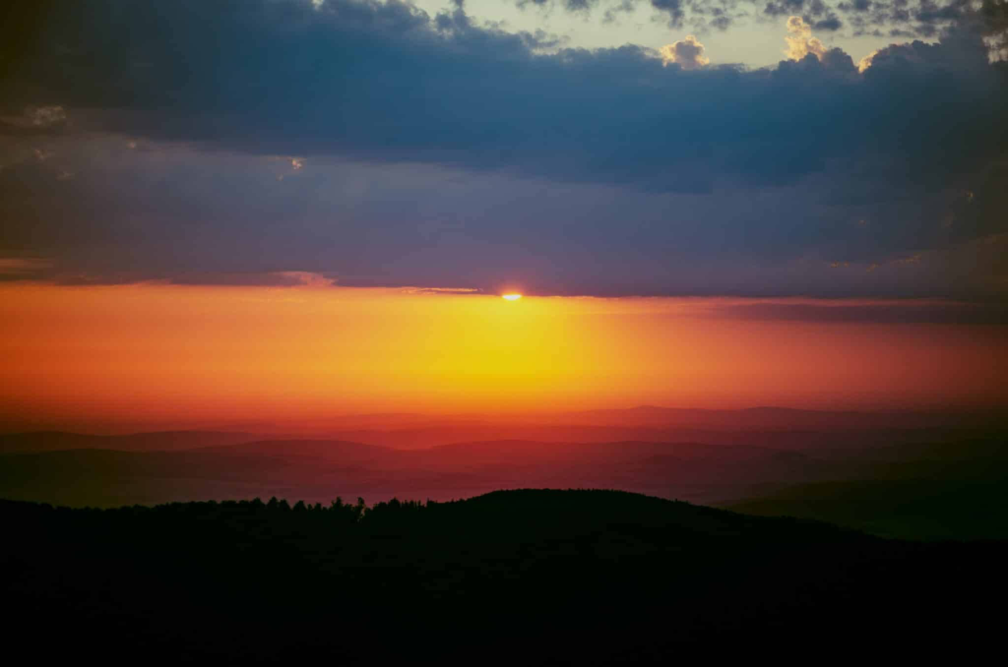 Beautiful orange and yellow sun covered by clouds in mountains