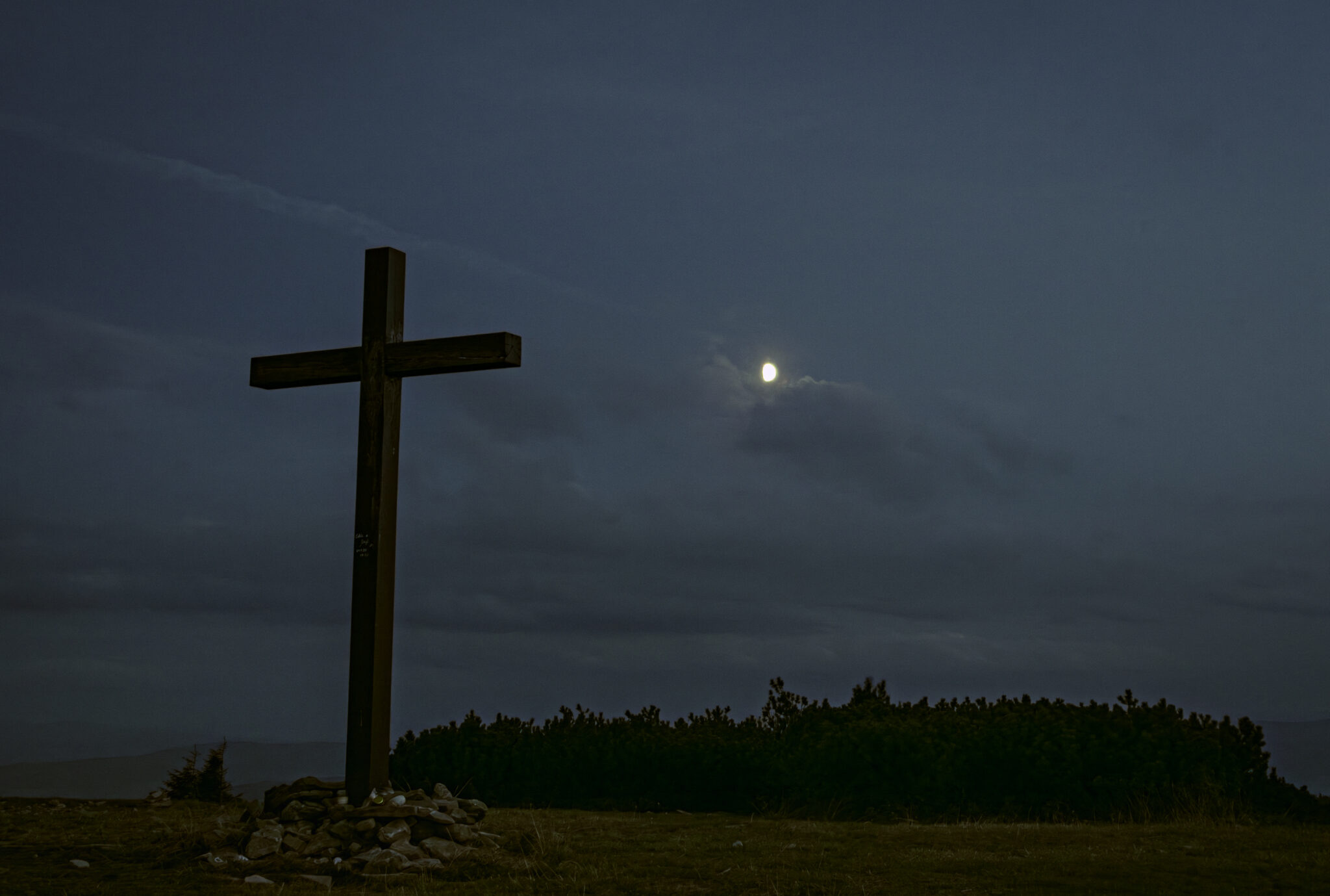 the moon gently illuminating the cross at the top of the mountain