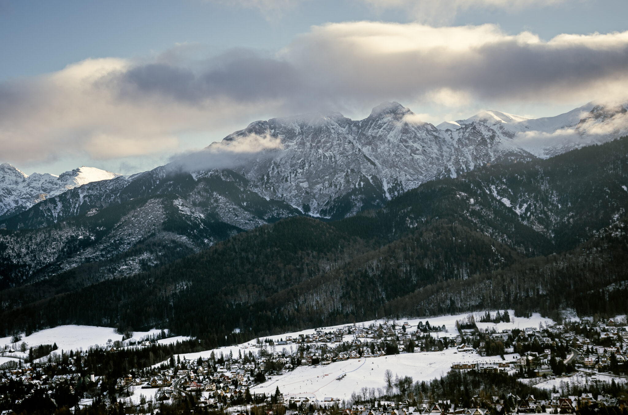 snow-capped mountains shrouded in clouds at sunset and a snow-covered town in the valley