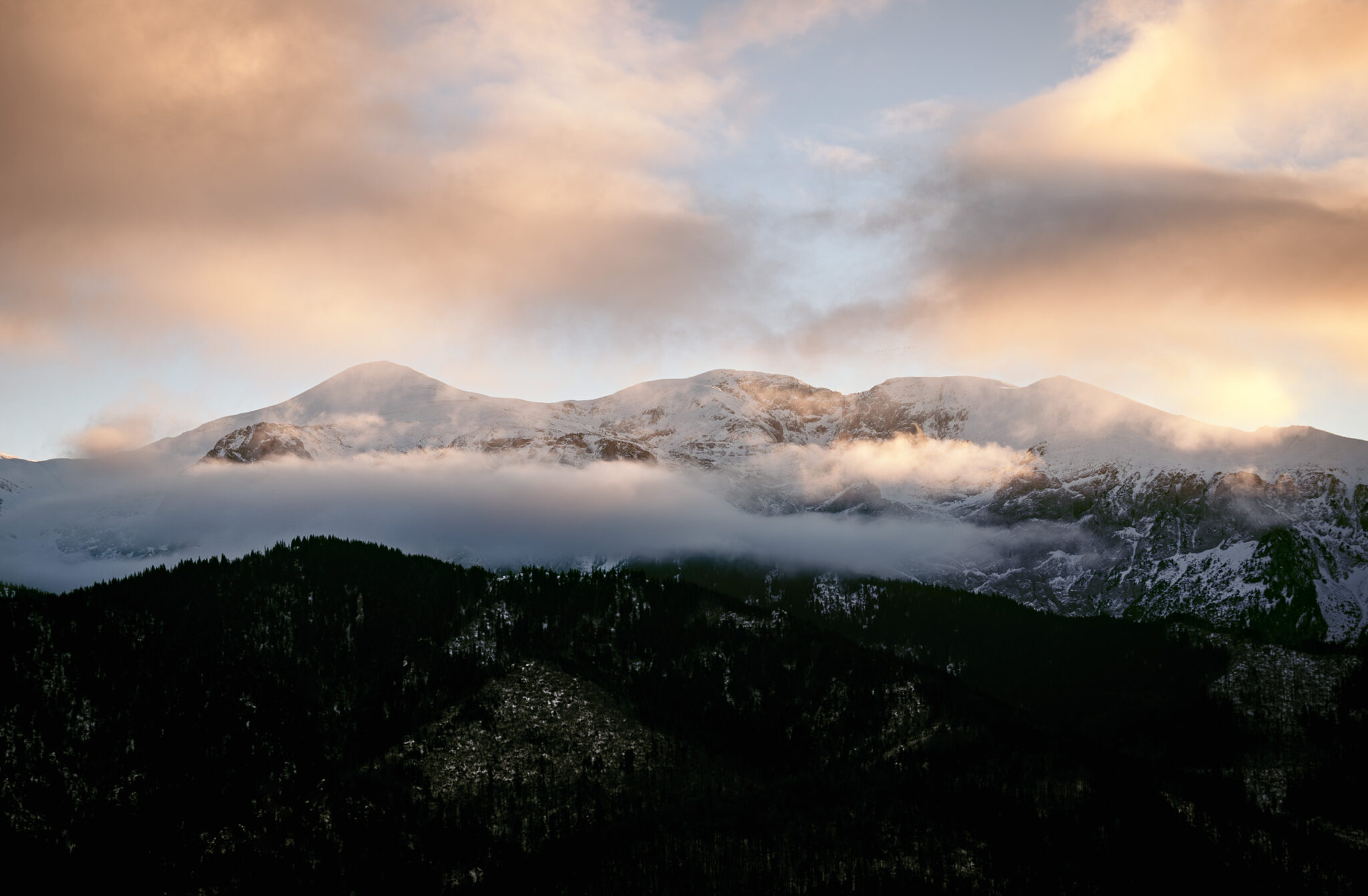 snow-capped mountains shrouded in clouds at sunset
